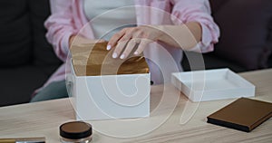 Close up view of female hands unpacking gift. Crop view of woman open white box standing on table with cosmetic on it