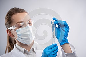 Close-up view of female microbiologist in biohazard protective clothing looking for biological tube with vaccine. Research and