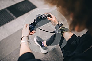 Close up view of female photographer holding digital camera while sitting on stair