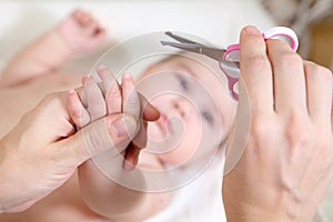 Close up view at fingernails cutting, mother with small scissors and her baby hand