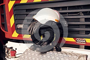 Close up view of firefighter's hat, gloves, jacket, pants and shoes. With big vehicle