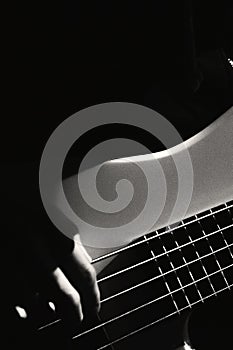 Close up view on five string bass guitar and fingers of musician lit by contrast light in dark room