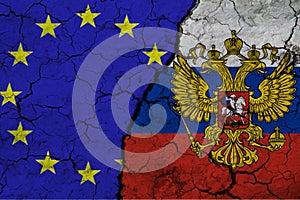 Close-up view of the flag of the European Union and the flag of the Russian Federation on a background of cracked earth. The