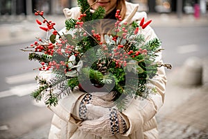 Close-up view of flower arrangement in pot of spruce branches and red berries and eucalyptus in female hands