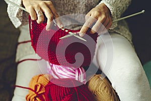 Close up view of fmale hands doing knit work with red wool. Handmade and hand craft clothes production in indoor hobby leisure