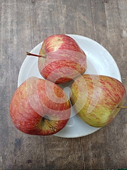 Close up view of fresh apples in a white saucer wooden background.