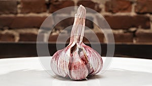 Close-up view of a fresh raw purple garlic bulb. Garlic bulb and garlic cloves on red brick wall background. Space for text