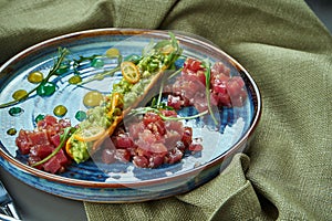 Close up view on fresh tuna tartare with bread, onion in blue plate on wooden background. Restaurant food. selective focus