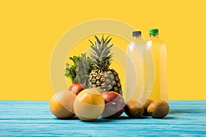 close-up view of fruity drinks in plastic bottles and fresh ripe tropical fruits on yellow