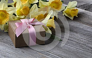 Close up view of a gift box with yellow daffodil on weathered wooden planks for Mothers day love holiday