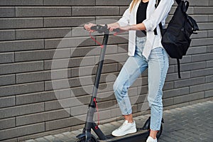 Close up view of girl in casual clothes that standing with electric schooter outdoors at sunny daytime