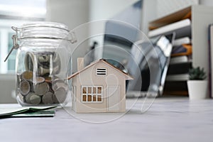 Close up view of glass jars with coins and house model on table. Planning savings money to buy a home, Real estate and property.