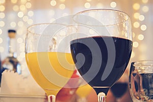 Close-up view of glasses with red wine and orange juice on a table in restaurant at the garlands curtain background. Filled glasse