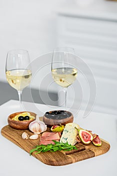 close-up view of glasses of wine and delicious snacks on wooden board on table