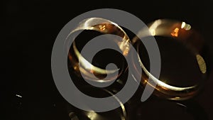 Close-up view of the golden wedding rings lying on the dark background. Beams of light are illuminating the rings.