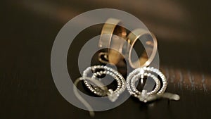 Close-up view of the golden wedding rings and silver bridal earrings with diamons at the table.