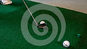 Close up view of the golf club at the ball on the green carpet mat at the driving range