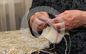 Close-up view of grandma`s hands holding knitting needles while sitting on the sofa, creating something with her own
