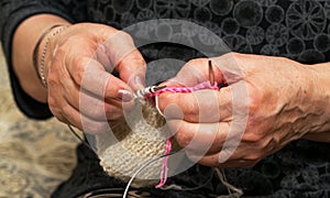 Close-up view of grandma`s hands holding knitting needles while sitting on the sofa, creating something with her own