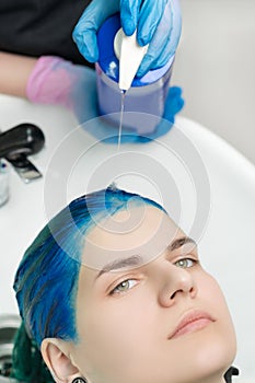 Close-up view of hairdresser squeezes shampoo from tube into head of woman with blue hair while washing hair in special