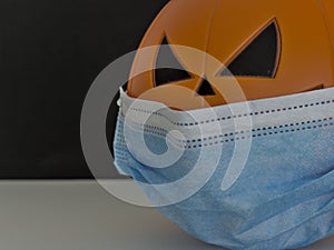 Close up view of Halloween pumpkin lantern wearing a medical facial mask as a symbol of disease control and virus infection and