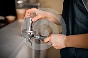 Close-up view on hand of barista tamping coffee in portafilter before making coffee in machine