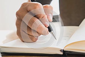 Close up view of hand holding a pen and writing on notebook diary