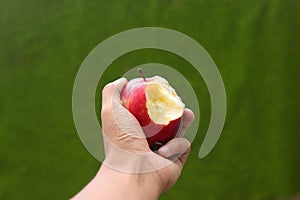 Hand holding half-eaten red apple with a green blurred background