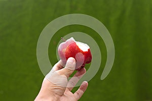 Hand holding half-eaten red apple with a green blurred background