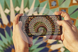 close up view of a hand holding a phone and taking a photo of a moroccan mosaic pattern at Hassan II mosque exterior - Casablanca