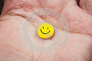 close up view of a hand holding a yellow pill with smiley face on it