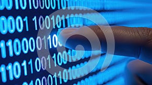 A close-up view of a hand interacting with binary code on a digital screen