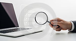 Close-up view of a hand using a magnifying glass over a laptop screen displaying code isolated on white background