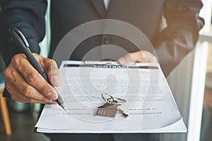 Close-up view hands of businessman signing leasing home documents and have a apartment keys on paperwork