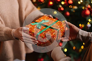 Close-up view hands of Caucasian young woman giving Christmas gift to African American man.