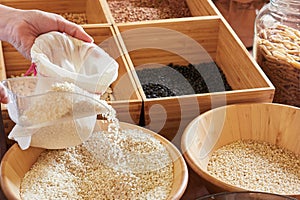 close-up view hands refilling reusable cloth bag with rice, bulk purchasing
