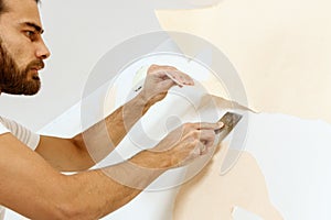 Close-up view on hands with a scraper in the process of removing wallpaper.