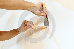 Close-up view on hands with a scraper in the process of removing wallpaper.