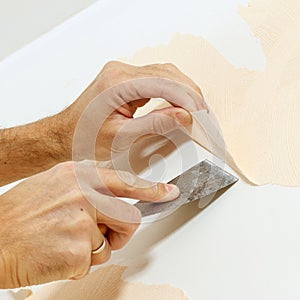 Close-up view on hands with a scraper in the process of removing wallpaper.