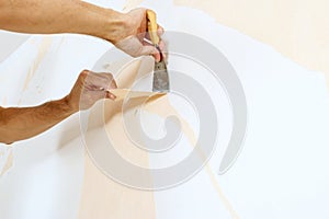 Close-up view on hands with a scraper in the process of removing wallpaper.