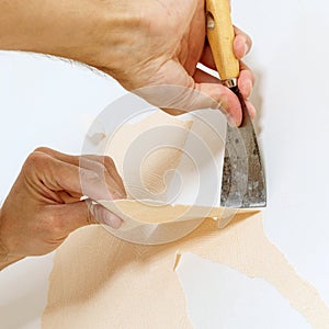 Close-up view on hands with a scraper in the process of removing wallpaper.