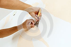 Close-up view on hands with a scraper in the process of removing wallpaper.