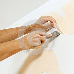 Close-up view on hands with a scraper in the process of removing wallpaper.
