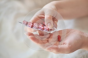 Close-up view of the hands of a sick young woman. Girl in bed holding blister and tablets or pills. Blurred background