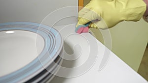 Close up view of hands in yellow gloves cleaning white shelf of cupboard first with sponge then with cotton swab.