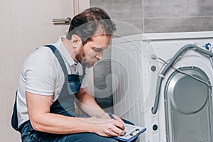 Close up view of handyman writing in clipboard and checking washing machine photo