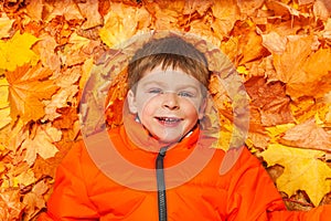 Close up view of happy boy laying on autumn leaves