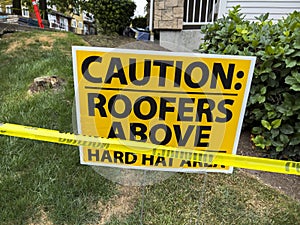 Close up view of a hard hat area sign with caution tape outside of a roof construction zone