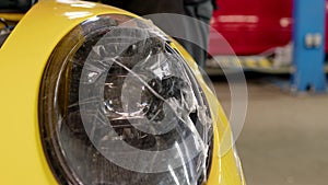 close up view of headlight of sport yellow colored car with broken glass. car after traffic accident in service repair