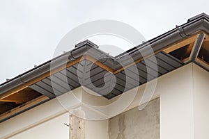 close-up view of a house with a gray roof and plums and filing of roof overhangs with soffits of house under construction